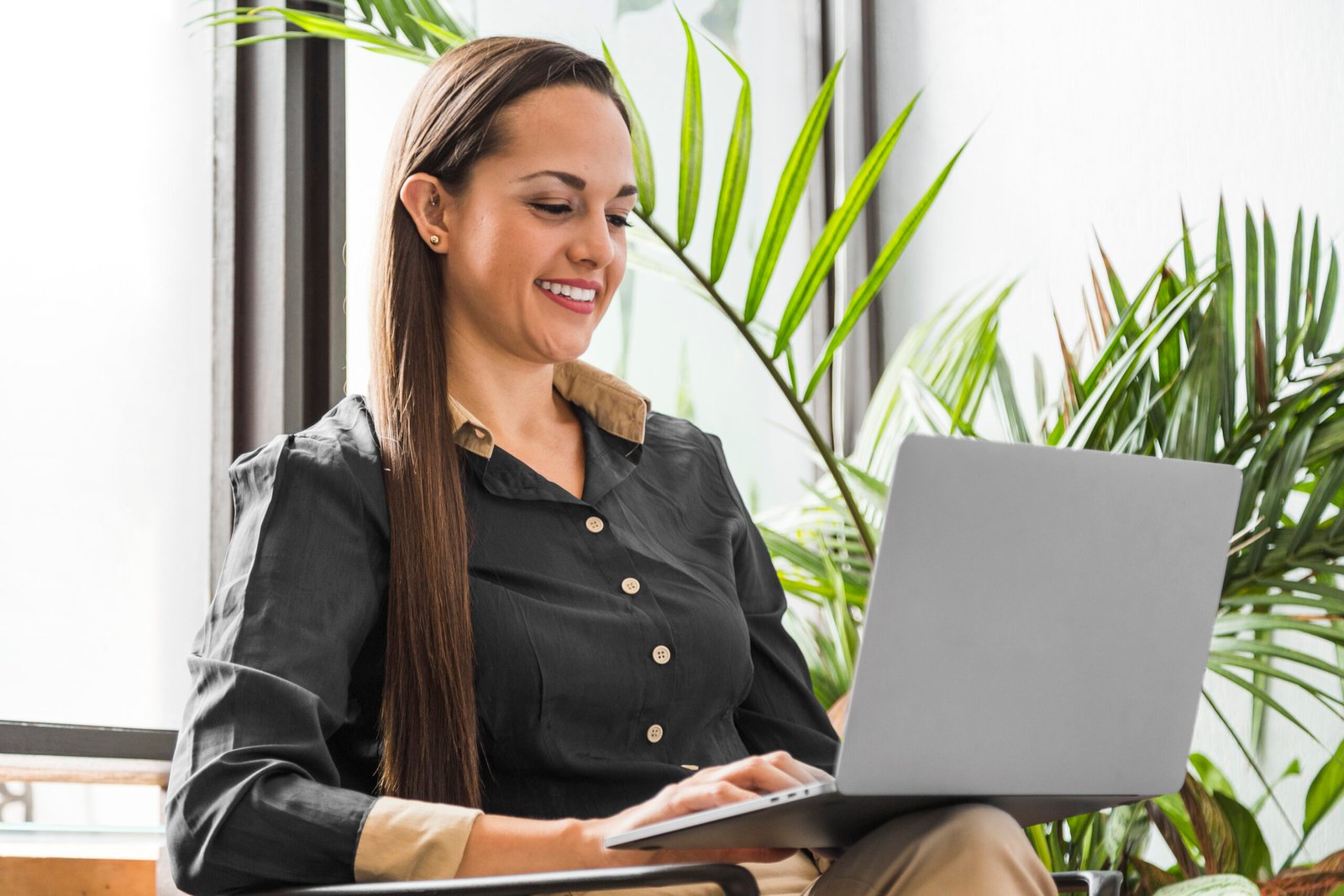 mulher com roupas sociais sorrindo e olhando para um notebook